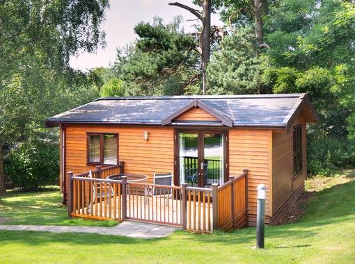 Pine lodge in the sunshine with trees behind and outdoor furniture with parasol