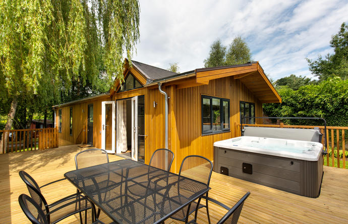 Exterior of Willow spa lodge with outdoor hot tub and outdoor dining furniture and willow tree to the side of the lodge